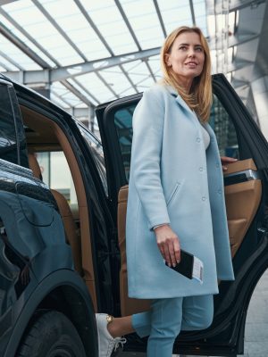 Smiling contented lady with travel document getting out of taxicab parked before airport terminal building